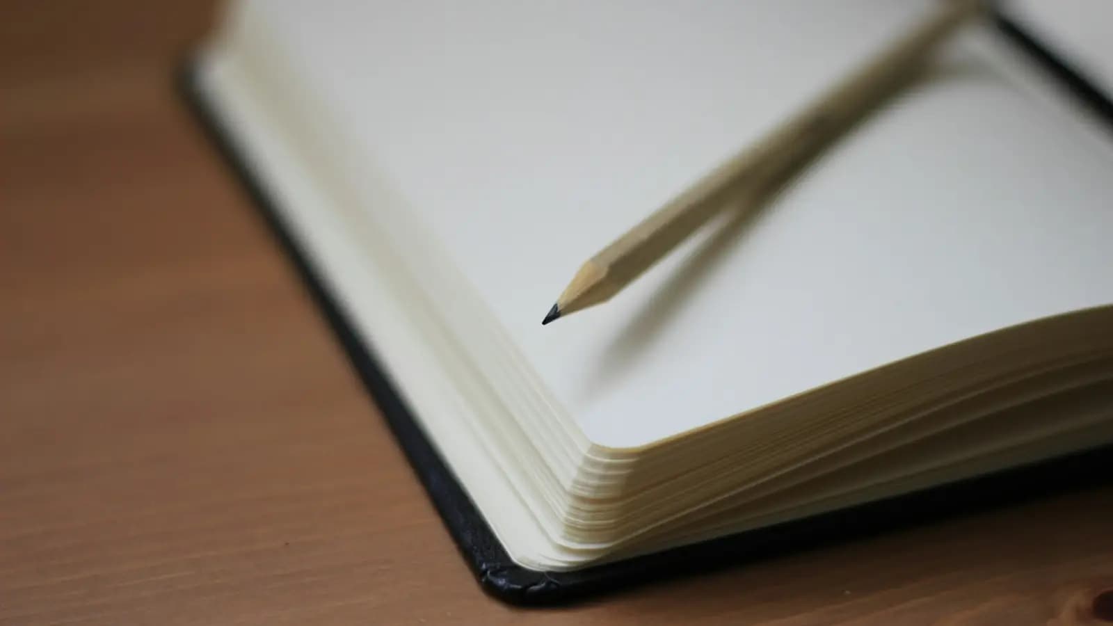 Carnet noir ouvert sur une table en bois, avec un crayon posé sur les pages blanches